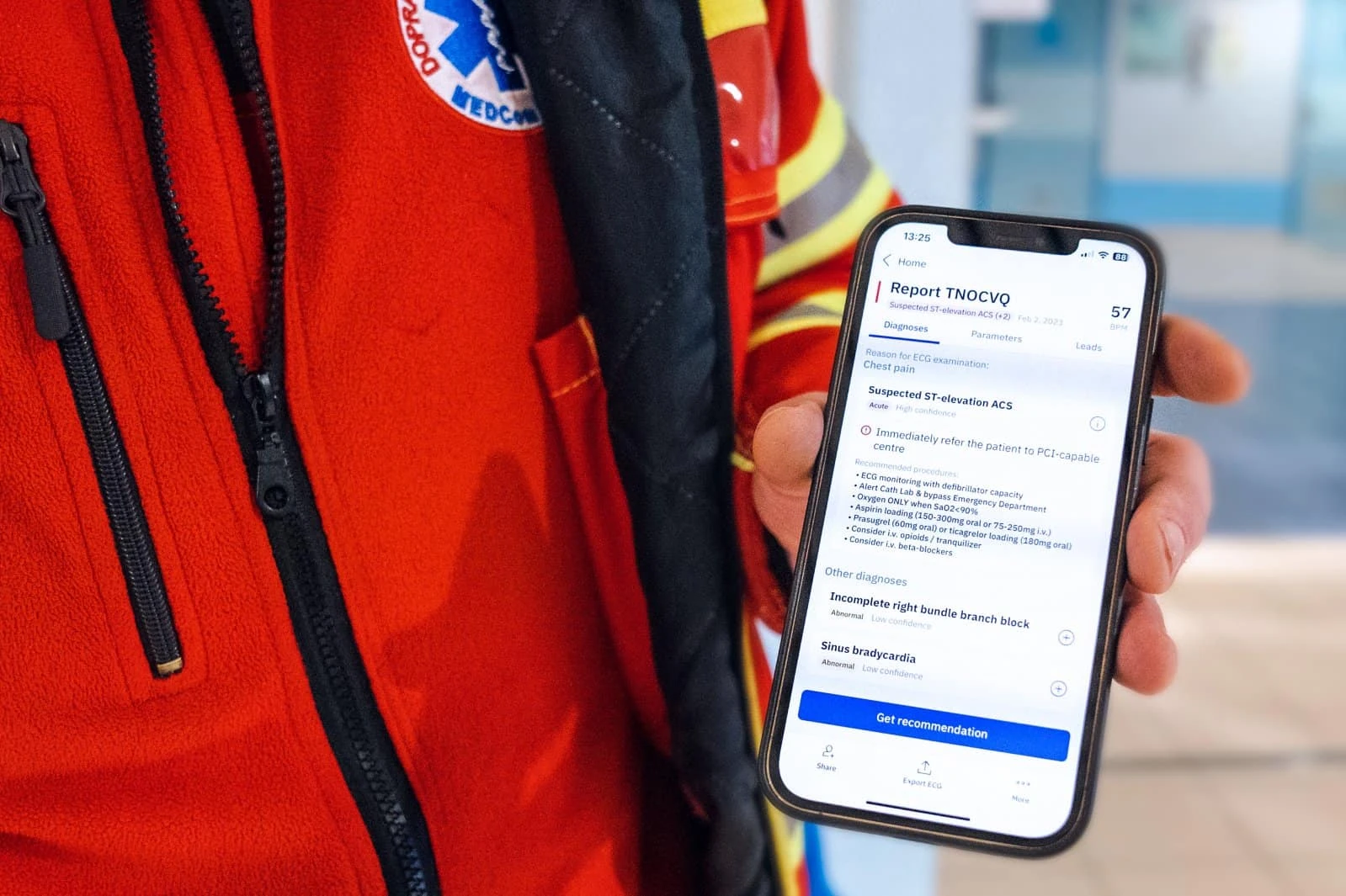 Paramedic holding a phone showing a PMcardio report of suspected ST-elevation ACS with referral advice