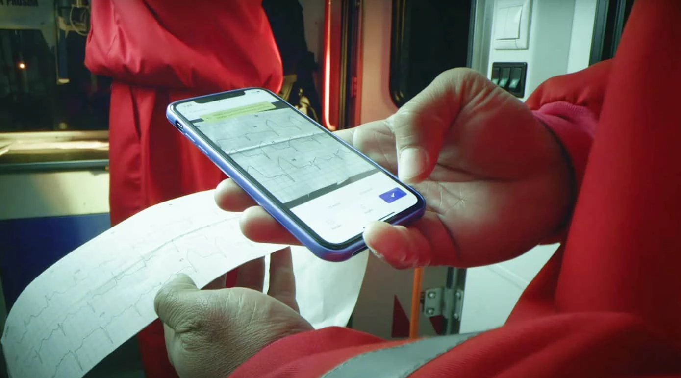 Paramedic scanning a paper ECG strip with PMcardio on a phone inside an ambulance