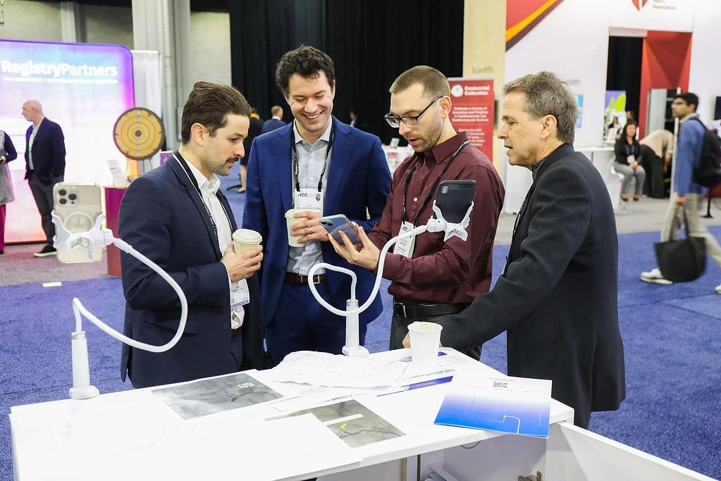 Cardiologists reviewing PMcardio ECG analysis on a smartphone at the ACC.24 exhibit booth