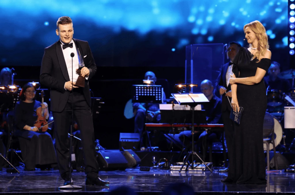 Martin Herman on stage holding his trophy beside the host at the Crystal Wing Award ceremony