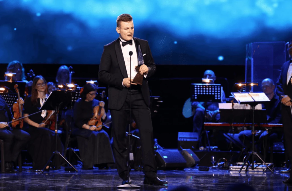 Martin Herman giving his acceptance speech at the microphone with orchestra at the Crystal Wing ceremony