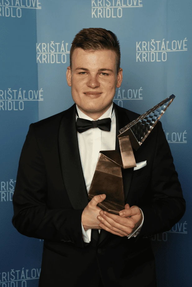 Martin Herman in a tuxedo holding the Crystal Wing Award trophy at the Kristalove Kridlo backdrop