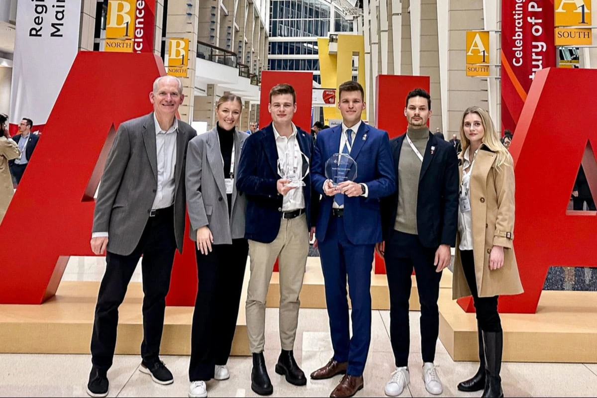 Powerful Medical team with AHA Health Tech Competition trophies before giant red AHA letters in Chicago